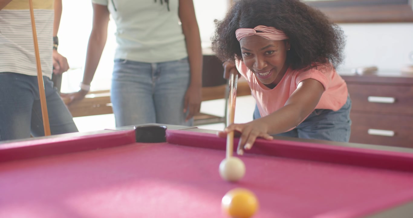 African American friends playing, woman in pink shirt lining up, striking cue on magenta pool table