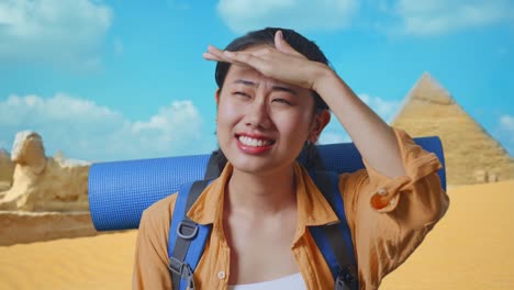 close up of asian female hiker with mountaineering backpack hand forehead smiling and looking distance while traveling in pyramid of giza