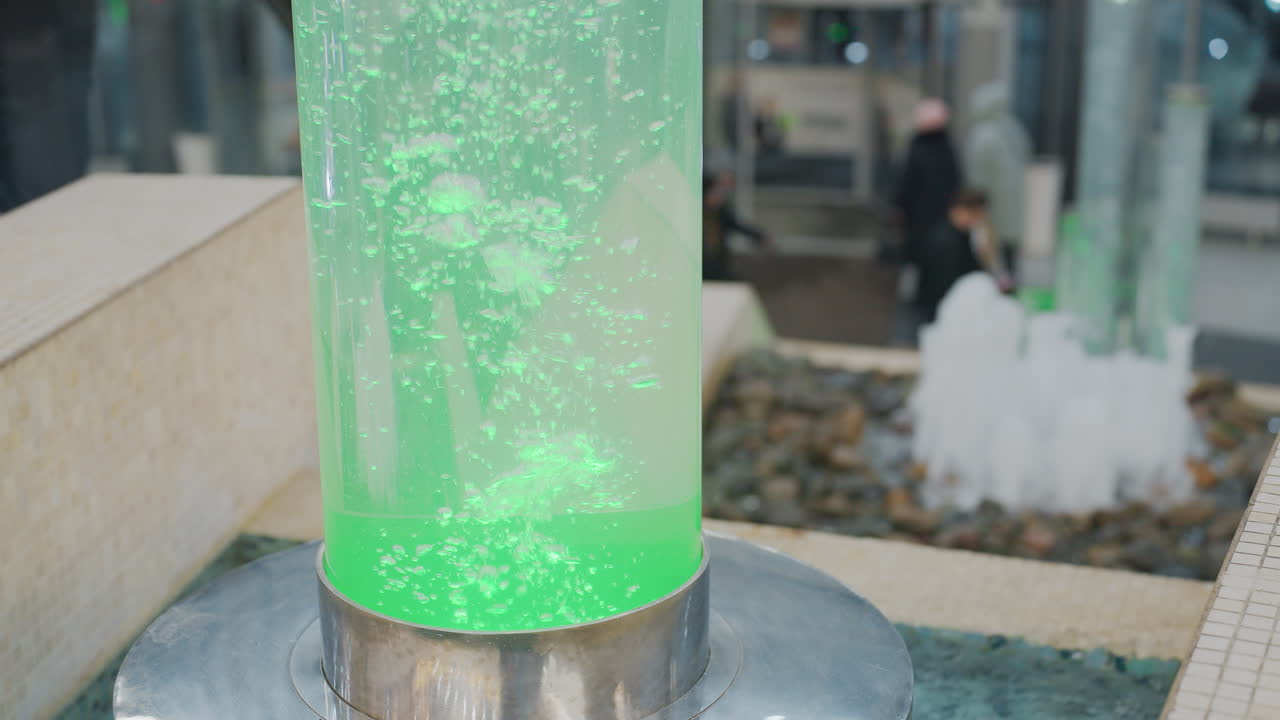 Beautiful Christmas decorations in mall with glowing Christmas lights, festive ornaments, and large cylindrical water feature in center, with blurred people in background