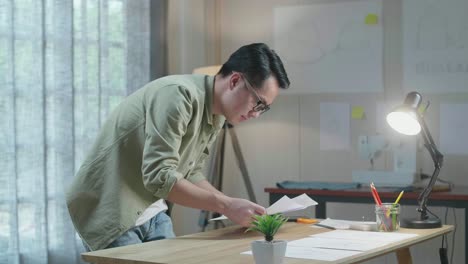 side view of asian man designer is arranging the layout bond on the table at the office
