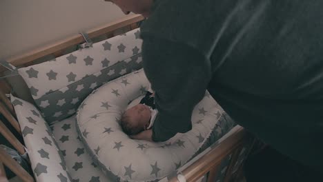 careful daddy puts sleeping baby in crib and sister at home
