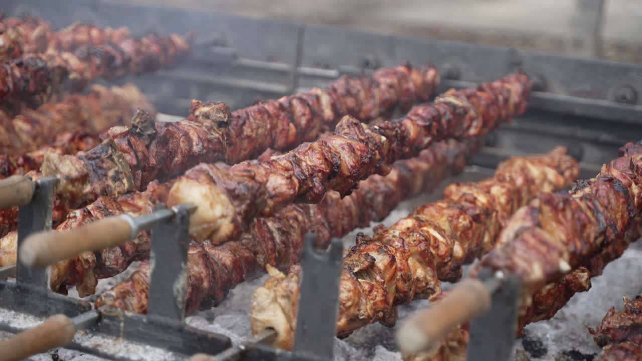 cerdo en primer plano y pinchos de pollo girando en un escupido sobre carbón caliente