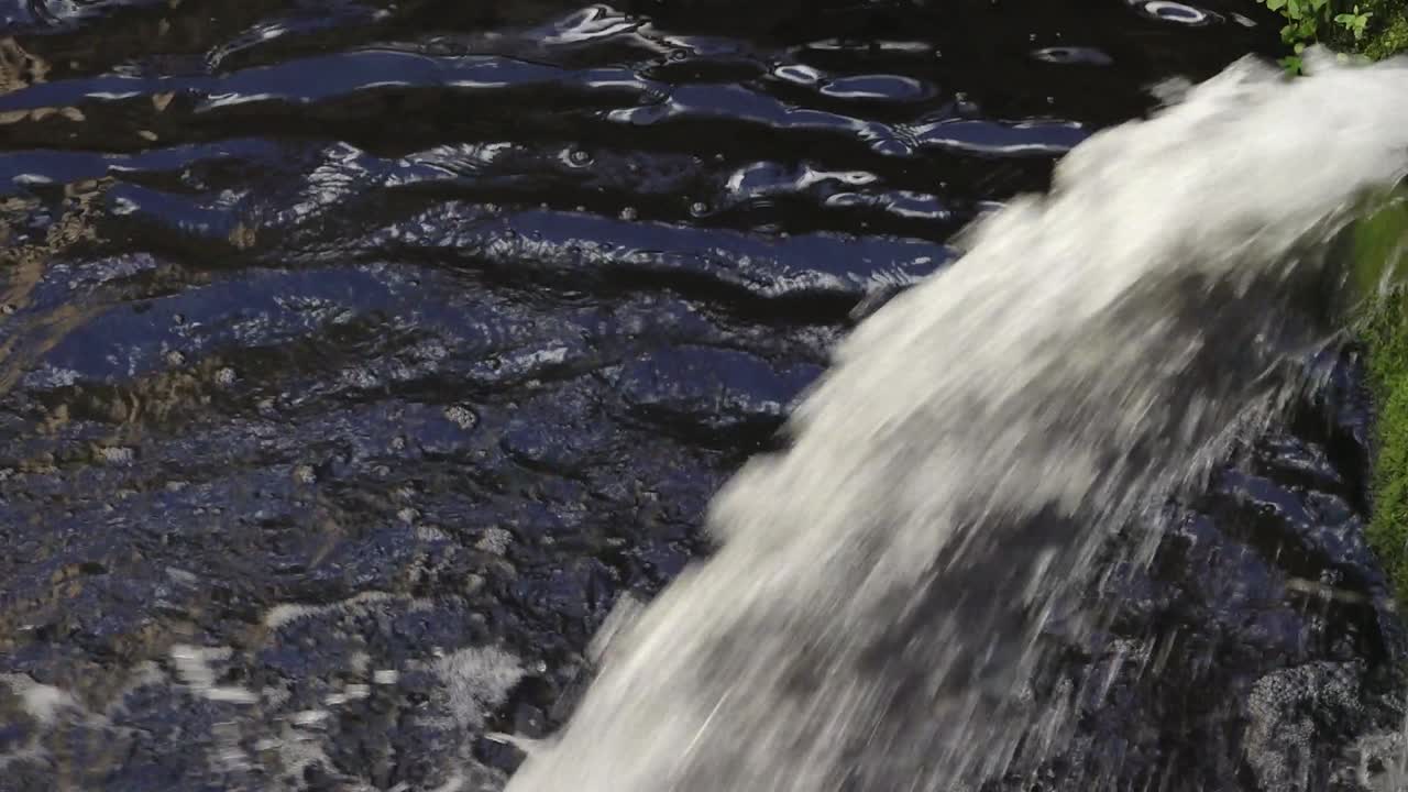 Water flowing strongly from a drainage pipe into a canal, creating ripples and foam on the dark surface of the water