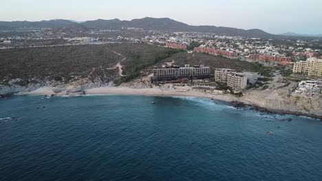 Vista-Aérea-De-La-Costa-Desde-La-Playa-Monumento-En-El-Hotel-Cape-Thompson-En-Los-Cabos-Con-Vista-Al-Malecón,-El-Mar-Azul-Con-Olas-Tranquilas-Y-Los-Terrenos-Del-Hotel-Durante-Unas-Vacaciones-En-México