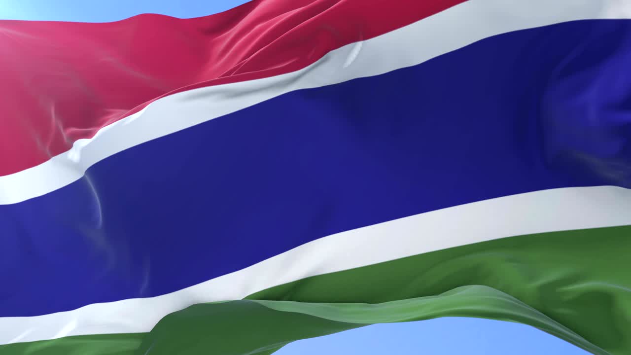 Gambian flag waving at wind in slow in blue sky, loop