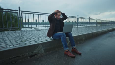 upset man working on laptop outside on sidewalk