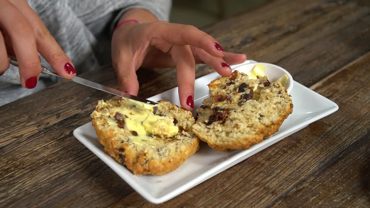slowmo - mujer joven esparciendo mantequilla en el tradicional bollo casero de nueva zelanda en un elegante café