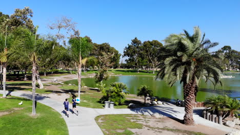 fly in-dolly behind igh school cross country runners at lake at mason regional park in irvine, ca shot by aerial 4k drone