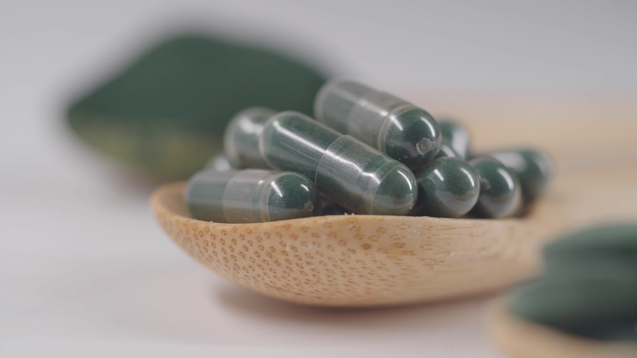 Green Herbal Supplement Capsules in Wooden Spoon