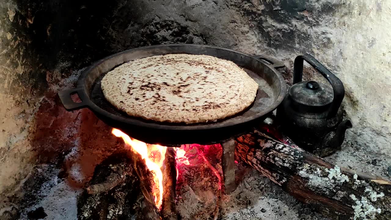 primer plano de cocinar pan en una sartén de hierro fundido descansando sobre salvamanteles, sobre un fuego de madera de roble en una gran chimenea de piedra en una cocina tradicional-4