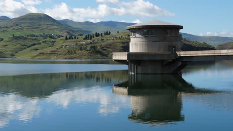 Intake-tower-reflects-in-sunny-day-reservoir-water,-Lesotho-mountains