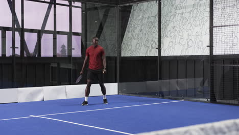 man playing padel tennis on indoor court, hitting ball with racket energetically