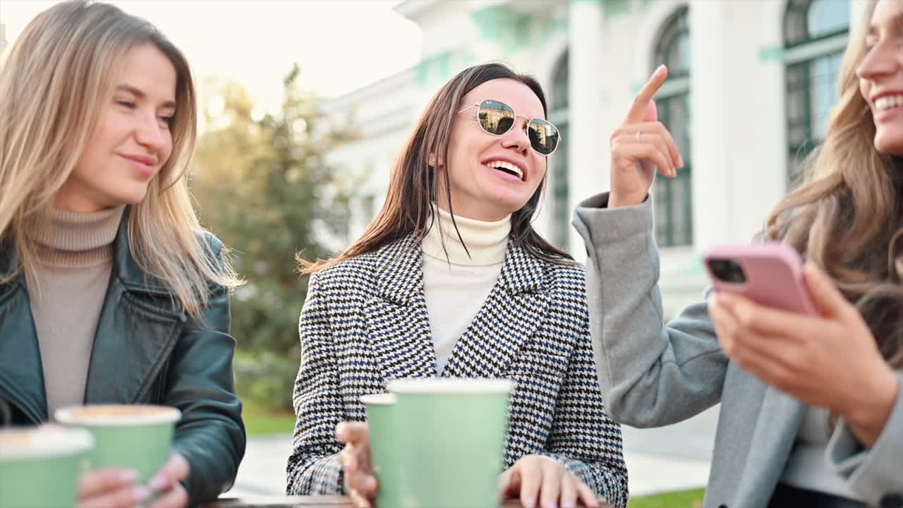 Three women going through a phone at a terrace