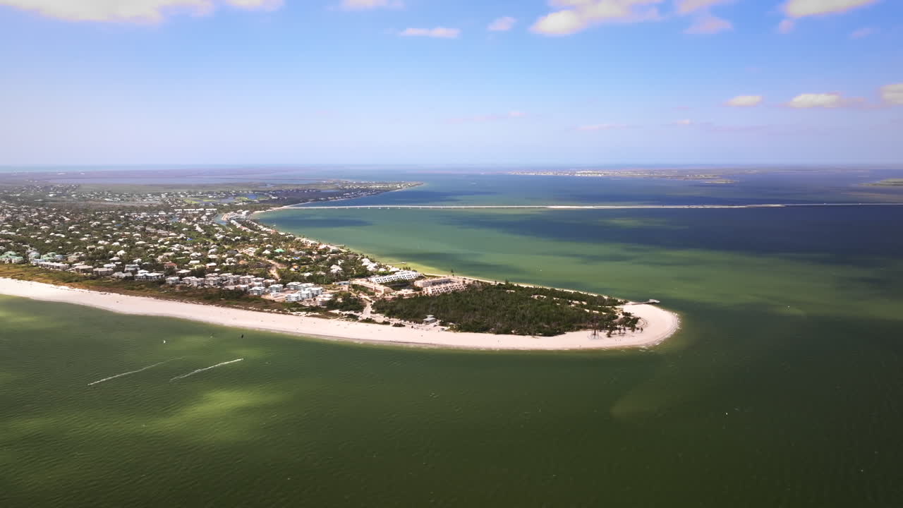Filmový, vysoko letící širokoúhlý letecký záběr dronem nad oceánskou stranou historického majáku na ostrově Sanibel a východním cípem ostrova Sanibel na Floridě, s jasným pobřežím.