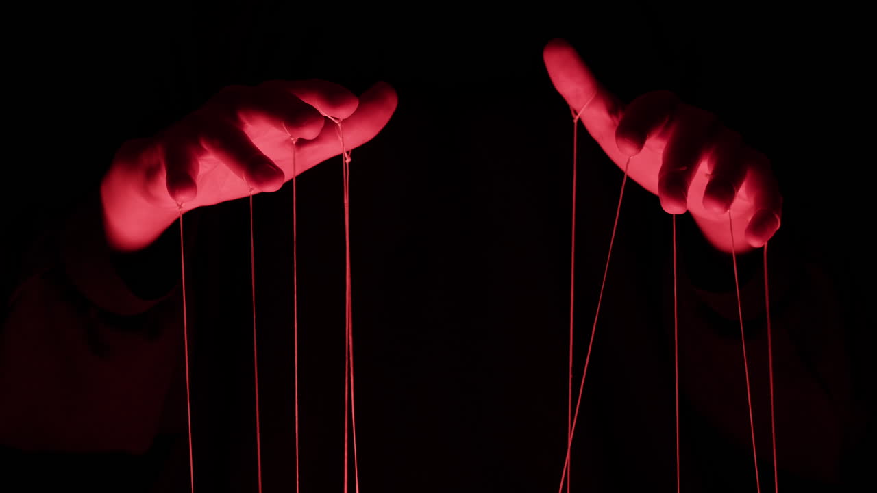 Red Lit Hands Manipulating Puppet Strings in Darkness