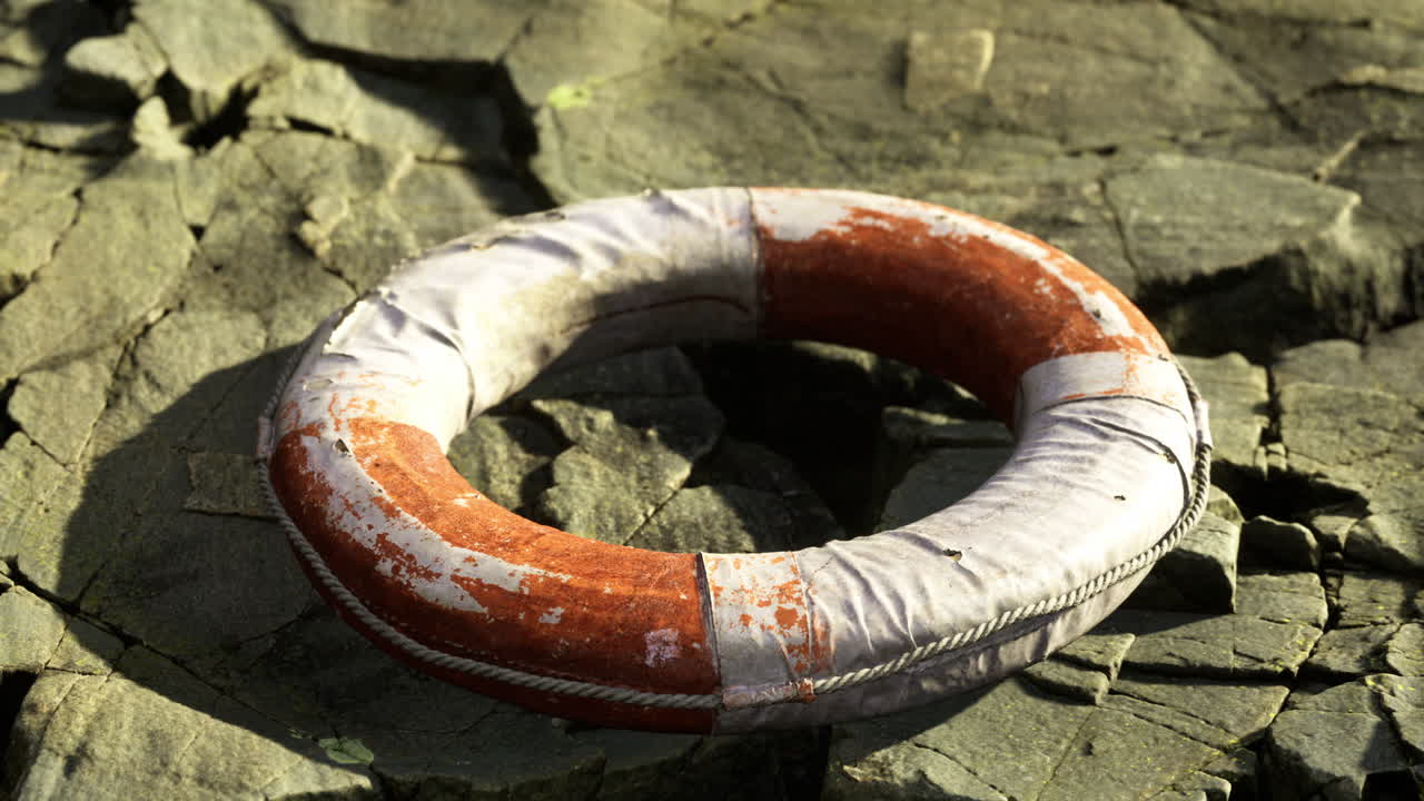 Life buoy resting on cracked stones by the water at sunset
