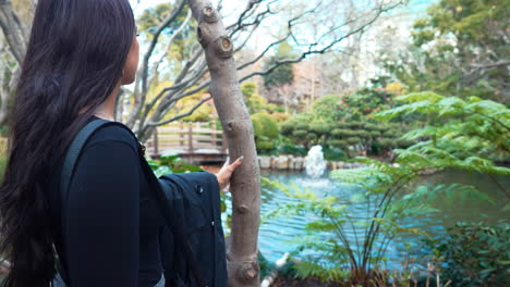 a slow-motion video depicting a beautiful young woman exploring a lush japanese tea garden with fountains and a bridge in san mateo, california