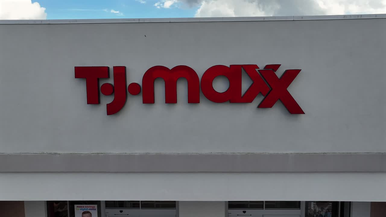 TJ Maxx Storefront Building in American shopping center. Clothing, handbag, home decor. Aerial backwards shot. Man with kid leaving shop.