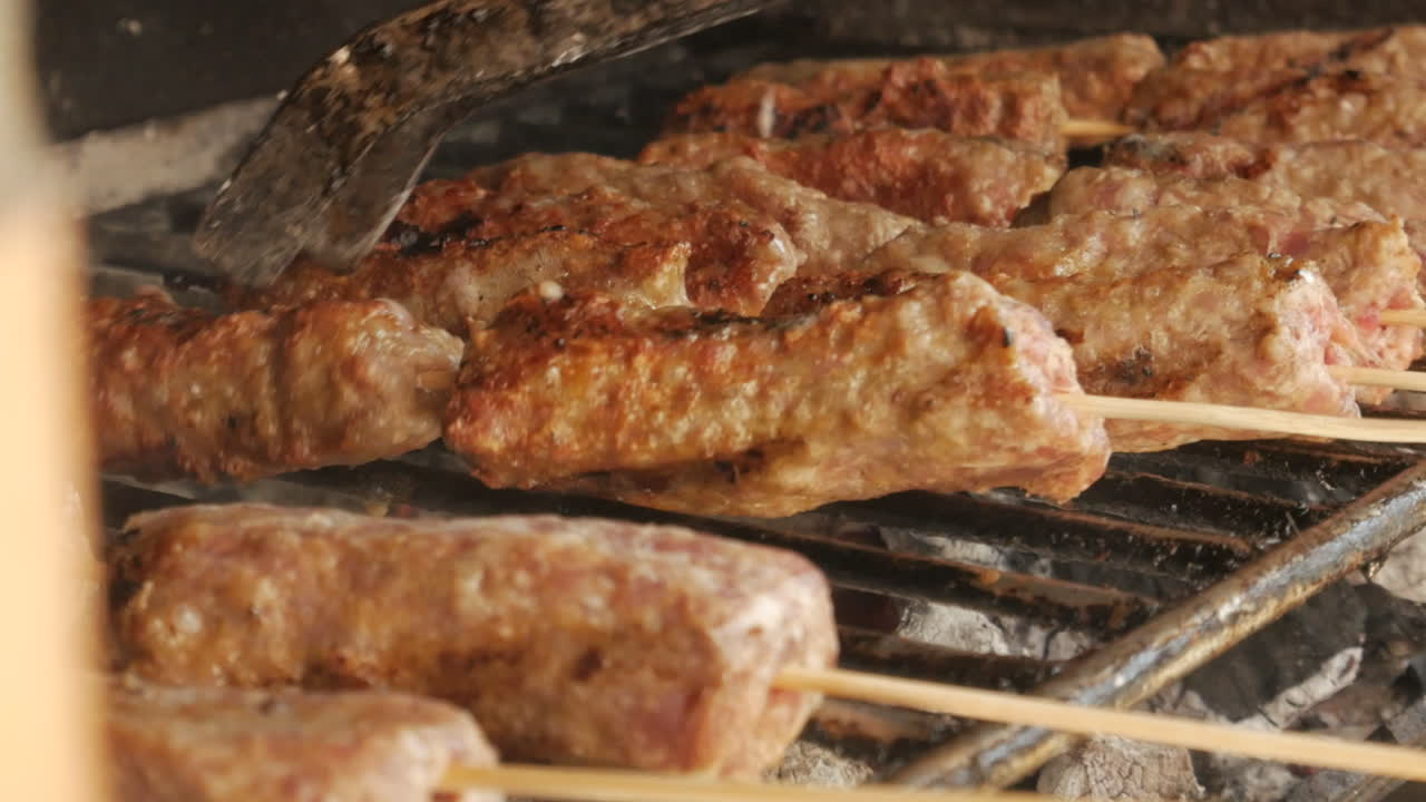 Primo piano di uno chef che gira Mici, tradizionale kebab rumeno, sul barbecue