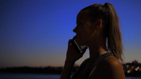 una mujer hermosa que detiene su trote nocturno en la playa de bondi, australia, para responder una llamada telefónica - lento