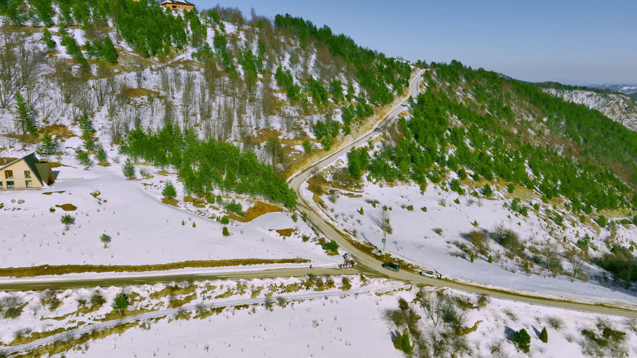 Aerial View of Winding Road in Snowy Mountain Landscape with Pine Forests and Houses