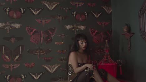 chica gótica con vestido brillante, maquillaje expresivo y mirada seductora, sentada en una habitación vintage oscura