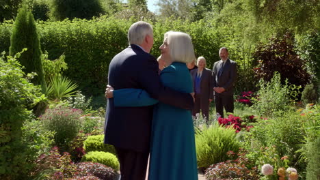 an emotional embrace between an older man and woman in a beautiful garden, surrounded by other people