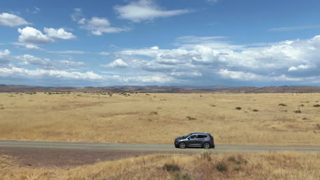 drone shot tracking a ev car driving in middle of remote prairie on a sunny day