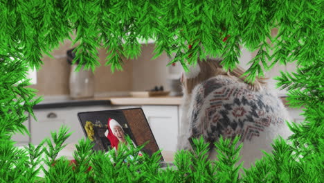 ramas verdes sobre una mujer con sombrero de santa haciendo una videollamada en una computadora portátil durante la navidad
