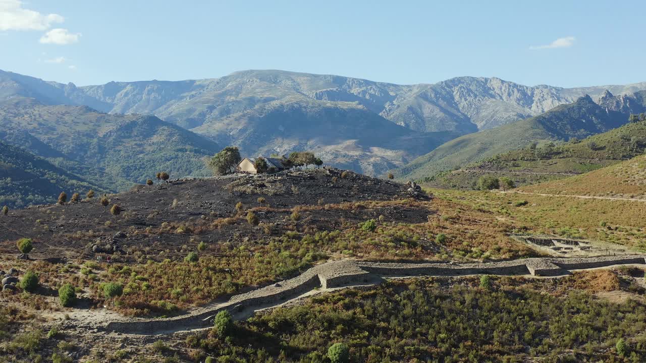 drone filming with parallax effect of the Vetton de el Raso Celtic fort, we appreciate part of its wall, a house and an area devastated by a fire, we enjoy its surroundings