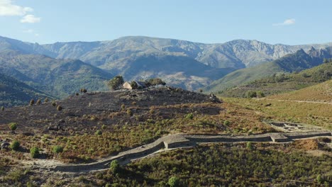 drone filming with parallax effect of the vetton de el raso celtic fort, we appreciate part of its wall, a house and an area devastated by a fire, we enjoy its surroundings