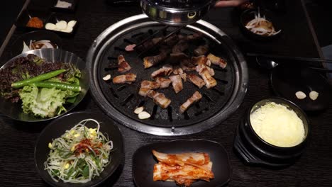 grilling pork belly barbecue with side dishes on the table - samgyeopsal set-up - close up, high angle