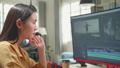 asian female video editor thinking while works with footage and sound on her personal computer in office