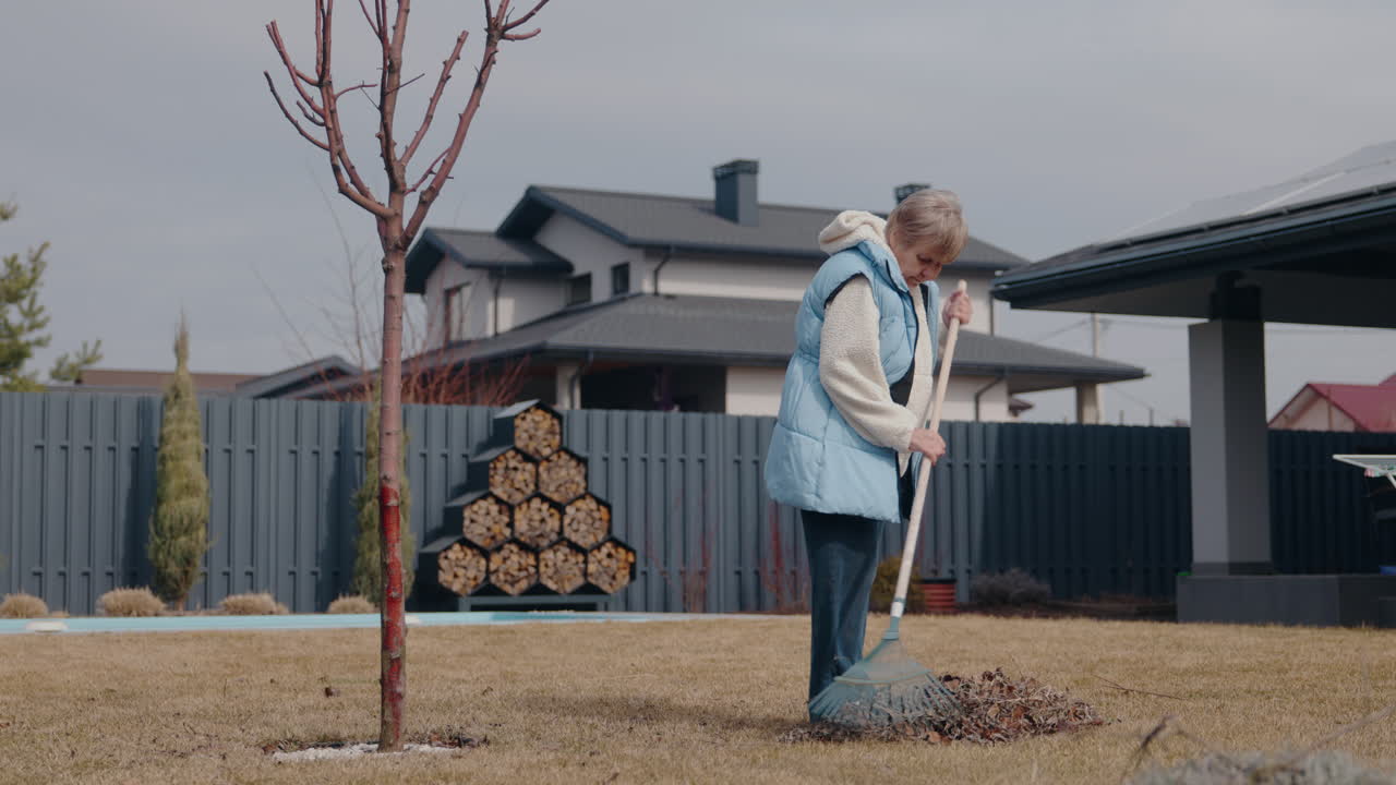 Senior Woman Raking Leaves in Backyard Garden