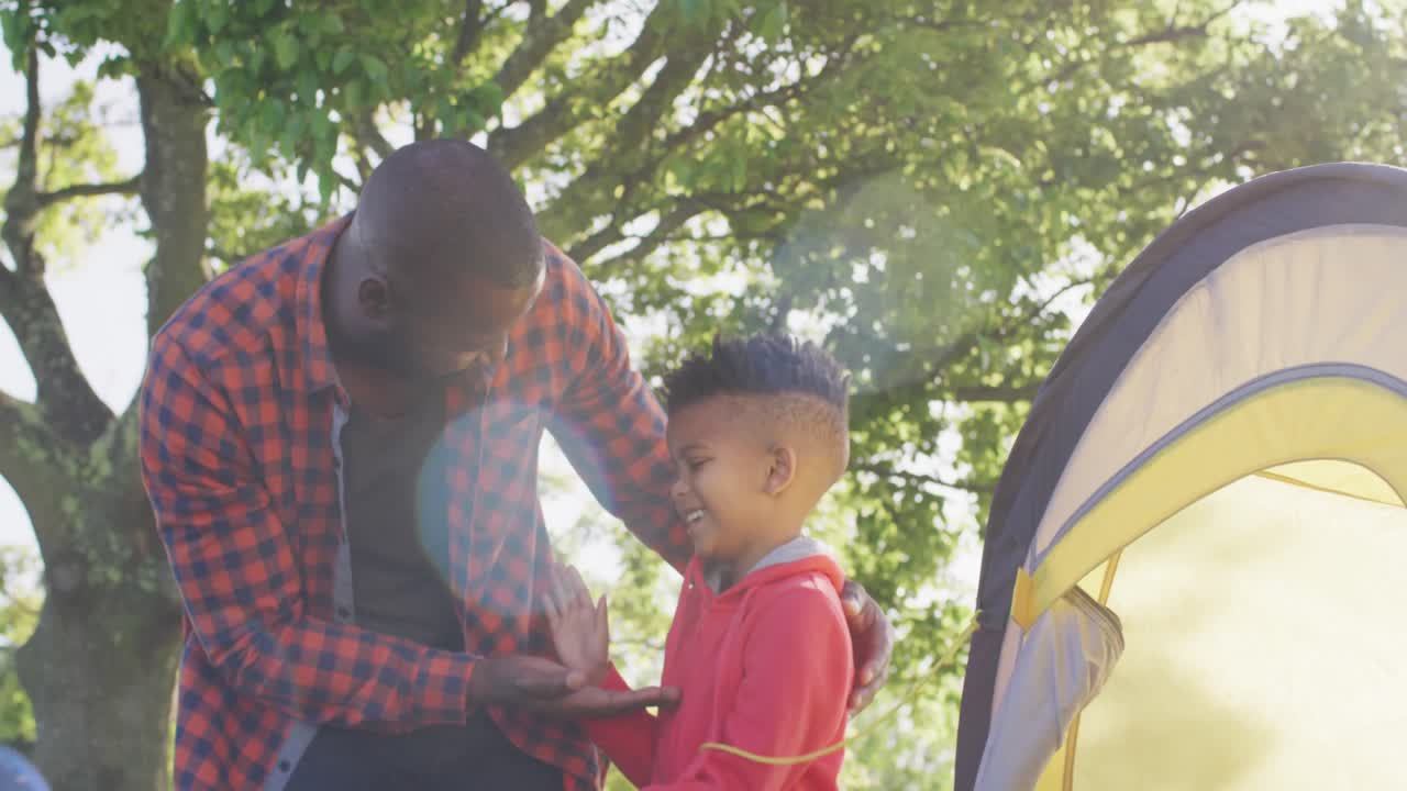feliz padre afroamericano y su hijo montando una tienda y dando cinco en el jardín