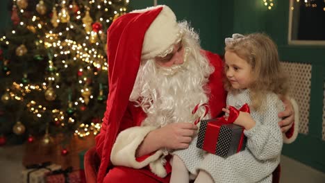 a girl joyfully sits on santas lap holding a candy cane a little girl joyfully sits on santas lap holding a candy cane a beautifully decorated christmas tree enhances the festive atmosphere