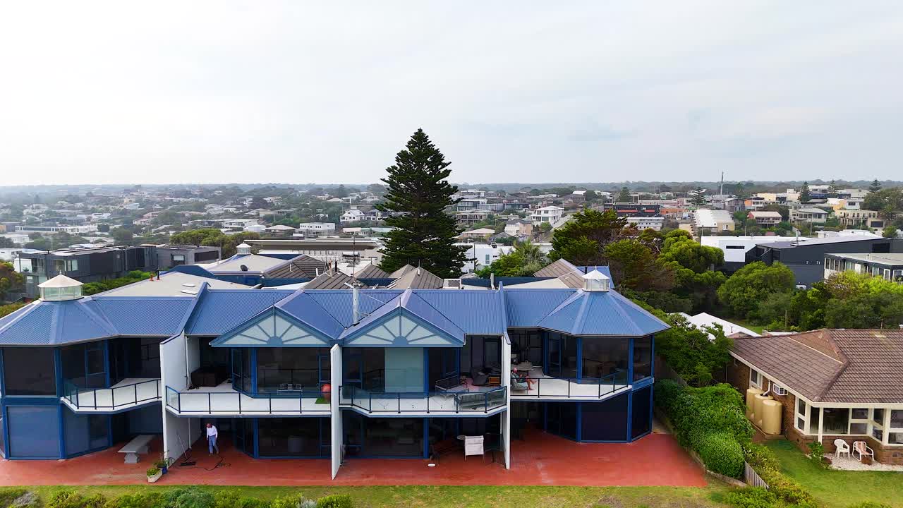 Drone footage captures a unique blue-roofed building in Ocean Grove, Victoria, with surrounding greenery and urban landscape