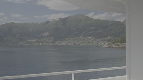 calm video filmed on board of a car ferry in norway going in between the fjords filming the mountains and sea or lake on a sunny cloudy day with a handrail in the foreground log