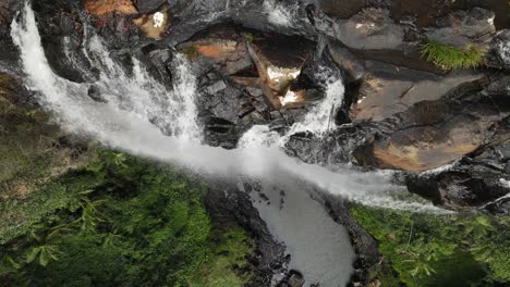 water flowing over the edge of a towering waterfall down into a naturally formed tropical swimming hole