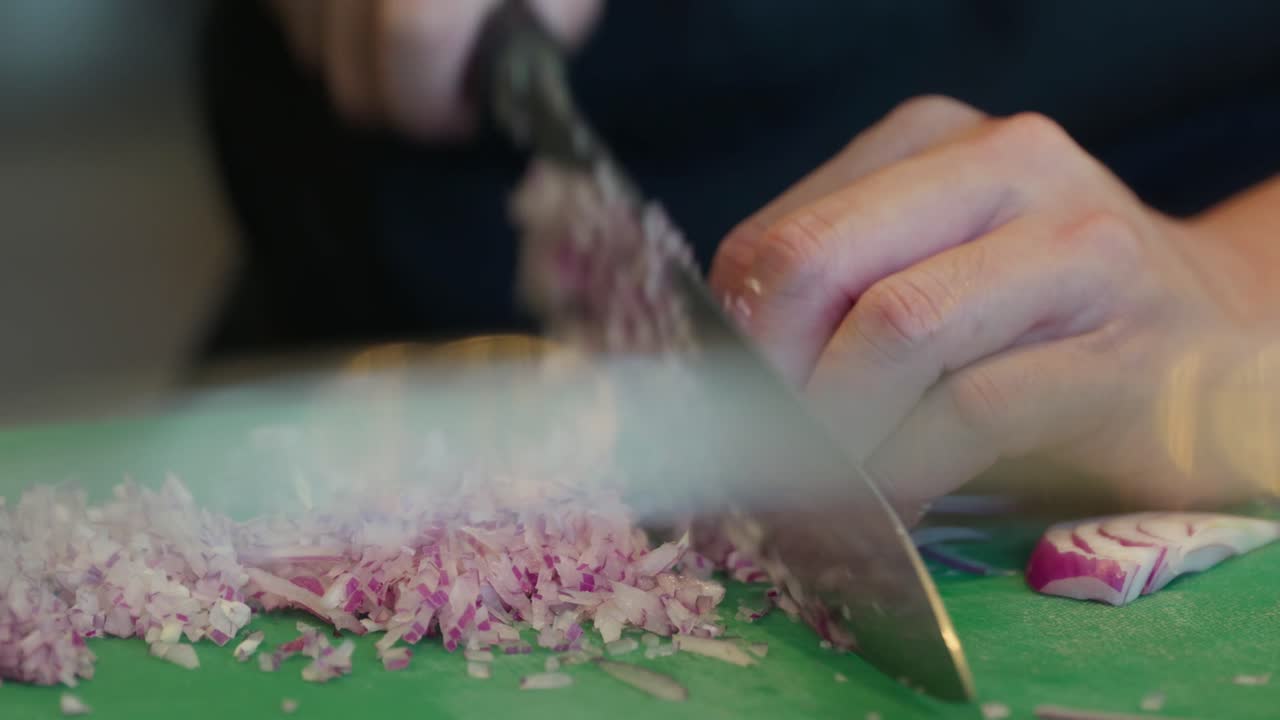 Close up, A chef finely dices a Spanish onion on a green chopping board with a very sharp knife