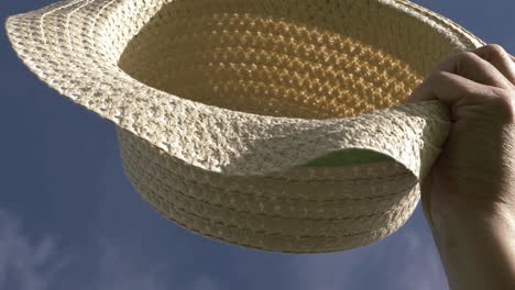 woman holding up straw hat against blue skies close up shot