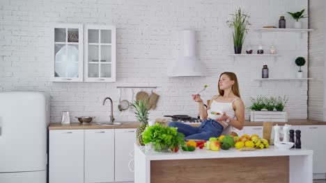 young woman is relaxing in the kitchen. beautiful girl sitting in the nice kitchen and eating fresh food. fresh organic fruit and vegetables. healthy food concept.