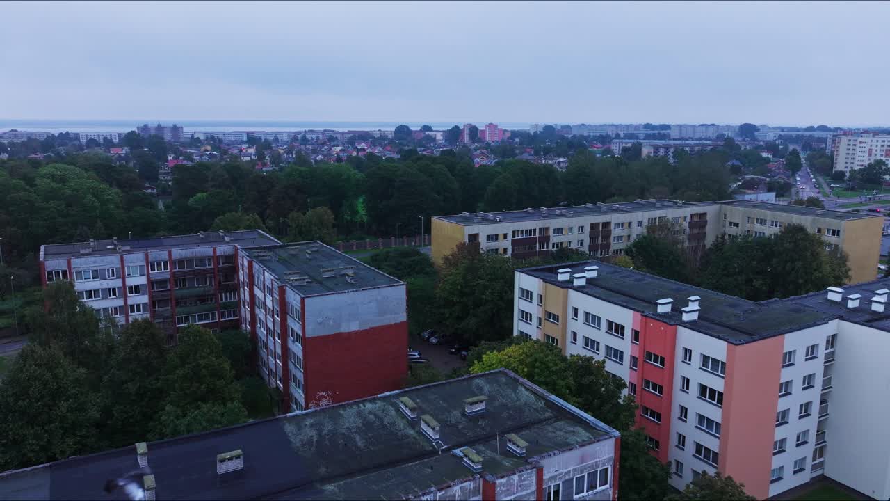 Flight ahead shows renovated and aging blocks, birds crossing frame, Liepaja