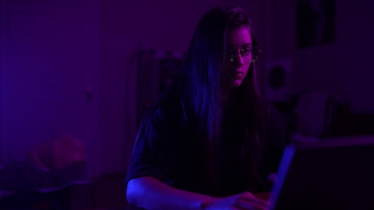 Person Working on Laptop in Night Room with Purple and Blue Lights