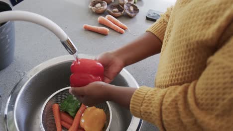 Sección-Media-De-Una-Mujer-Afroamericana-Enjuagando-Verduras-En-El-Fregadero-De-La-Cocina,-Cámara-Lenta