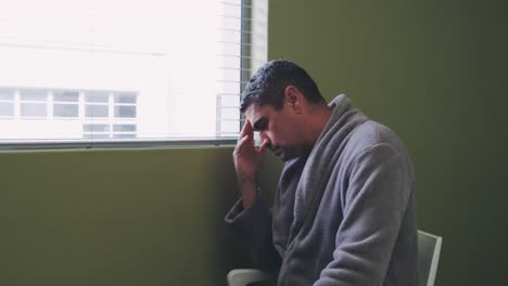 side view of caucasian male patient sitting near window in hospital ward 4k