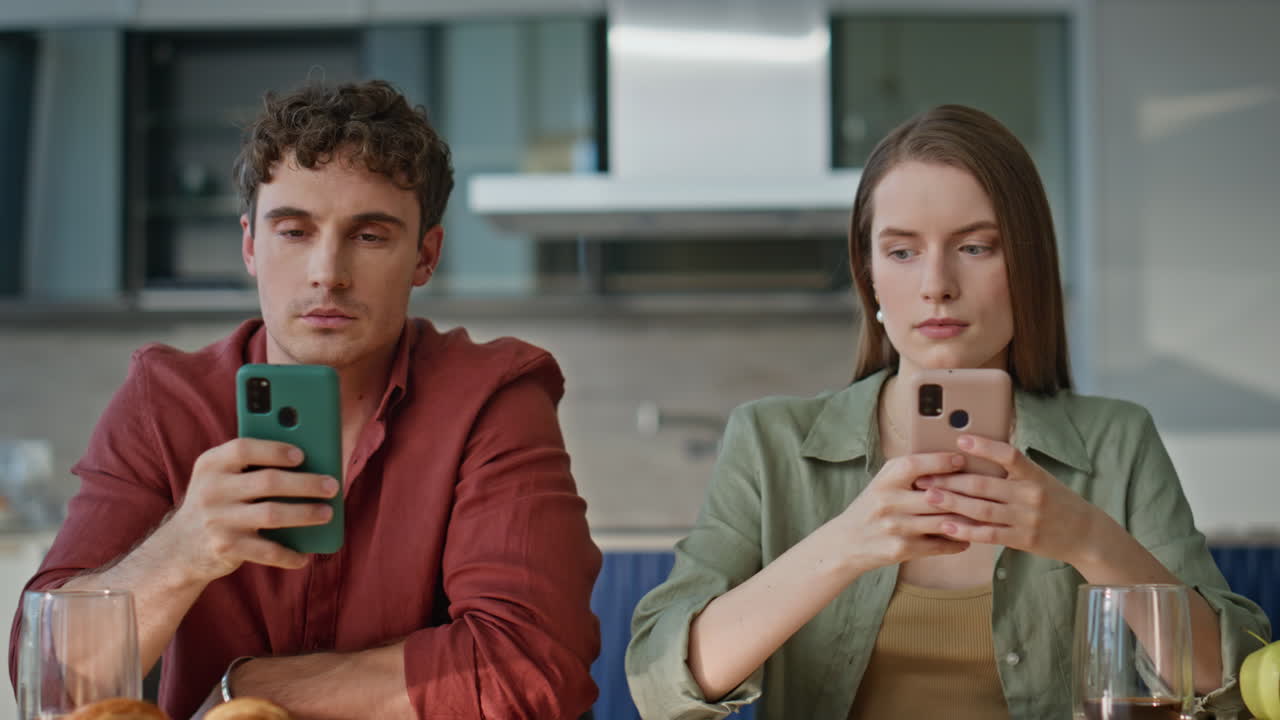 Couple cellphones sitting kitchen focused on gadgets at home breakfast closeup