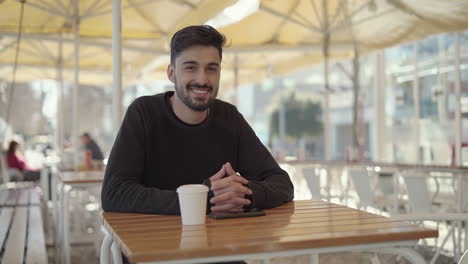 Man-using-smartphone-and-smiling-at-camera-in-cafe