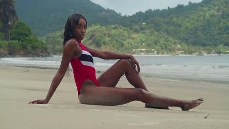 in trinidad, a young girl in a bikini sits in the sand and enjoys the tropical beach