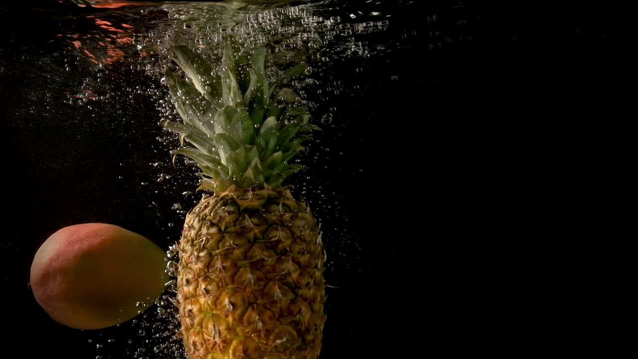 piña y mango cayendo lentamente en el agua clara y oscura